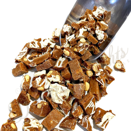 candy pieces with peanuts and white chocolate on a metal scoop against a white background